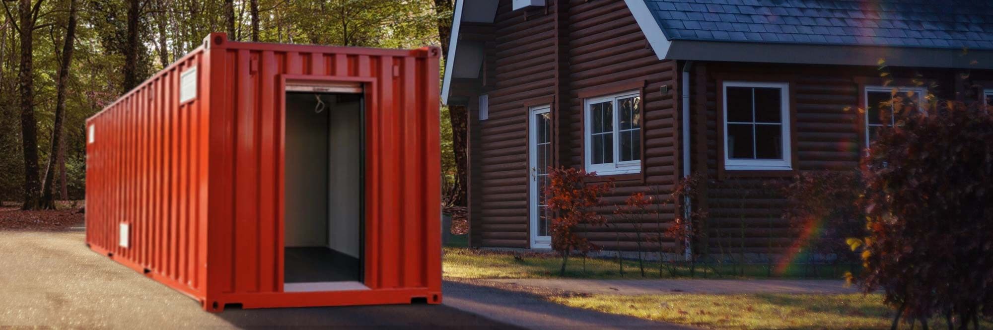 Orange shipping container with an open roll up door, sitting in the driveway next to a house with a forest in the background. 